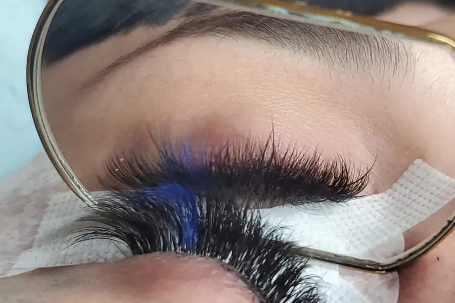 A dense, fluffy lash set with a streak of blue extensions, seen in a hand mirror held above the closed eye