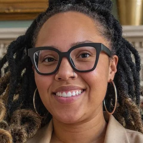 Desiree, smiling, in a beige blazer and hoop earrings