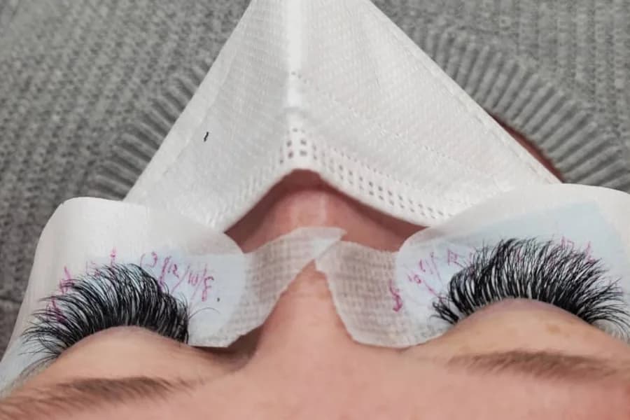 A full, dark lash set on a client lying back, with the lash map handwritten on her under-eye pads