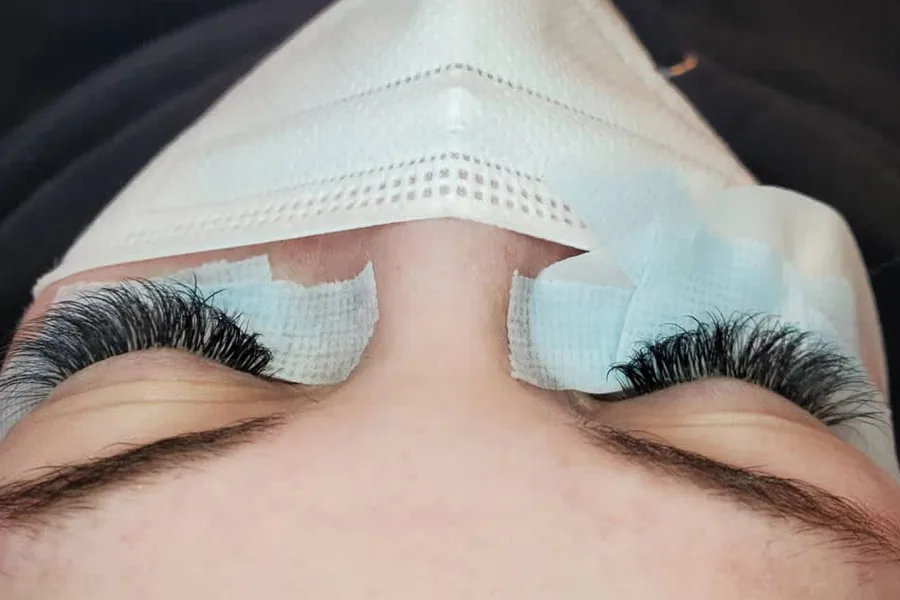 A full set of lash extensions on a client lying back with her eyes closed, under-eye pads still on