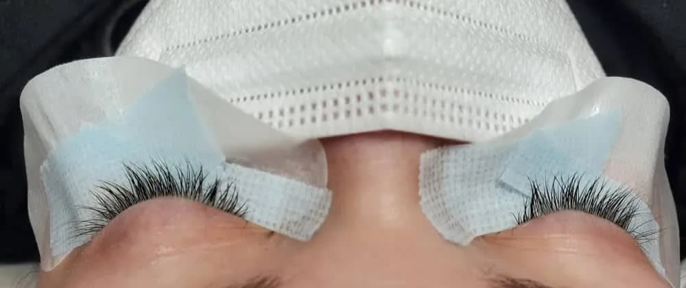 A soft, wispy lash set on a client lying back, her eyes closed and under-eye pads taped in place
