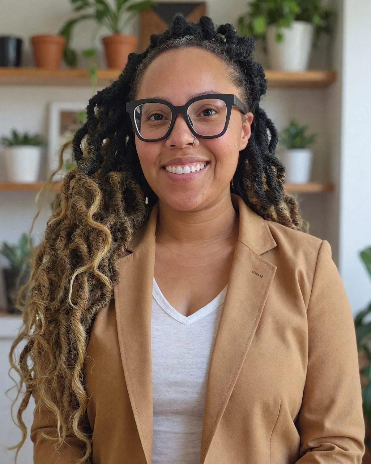 Desiree of Central Oasis smiling in a tan blazer, in front of shelves of plants