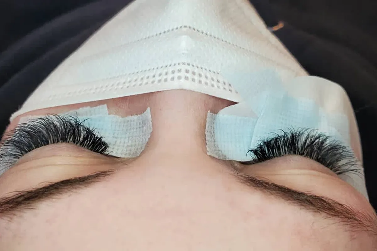 A full, dark lash set seen from above, eyes closed on soft under-eye pads