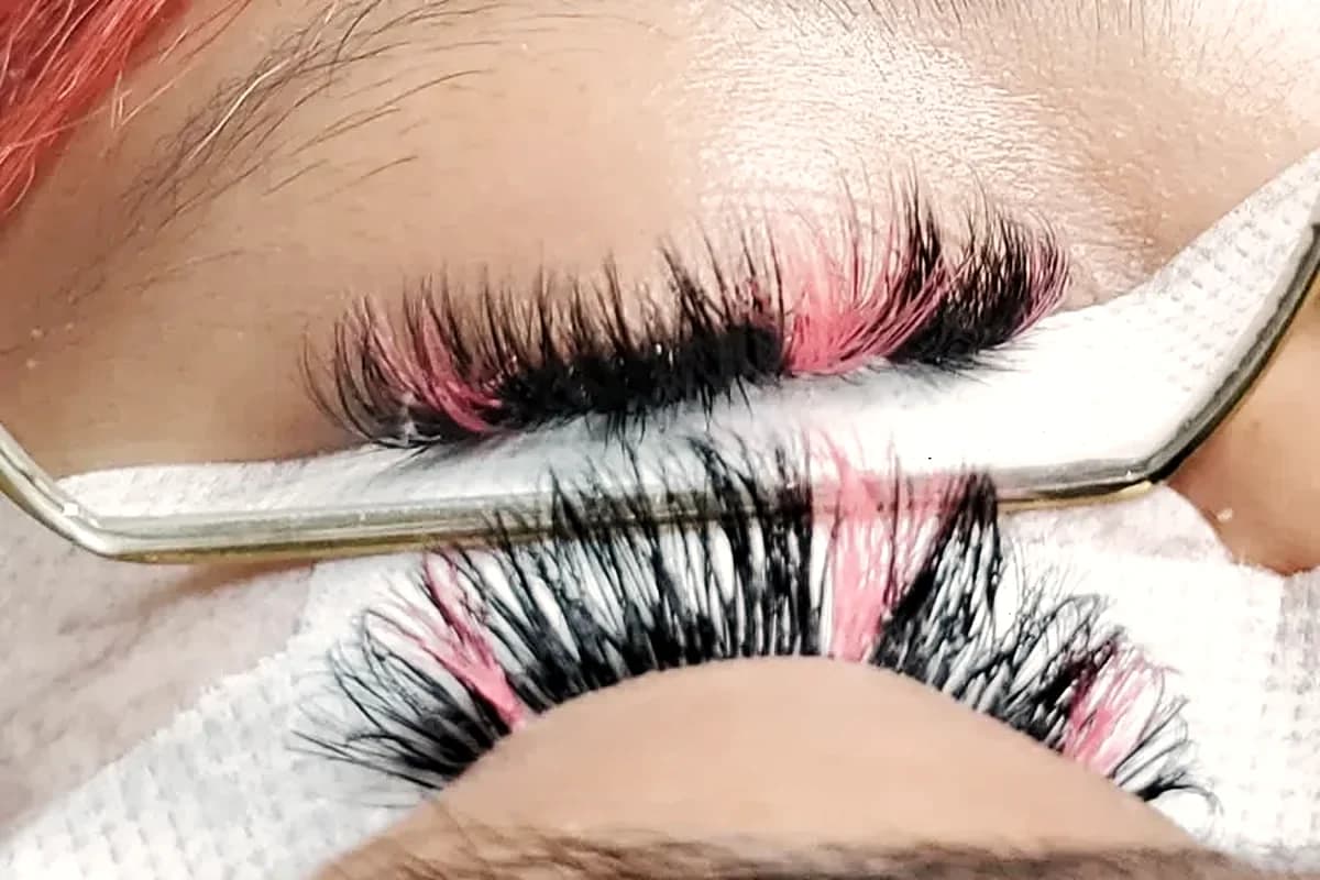 Fluffy lash extensions with pink color accents, held on under-eye pads during an appointment
