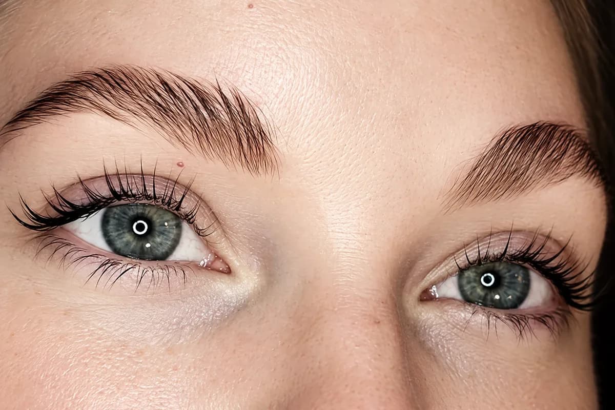 Brushed-up, feathered brows above a client's own lashes, curled up from the root and darkened, on both of her open green eyes