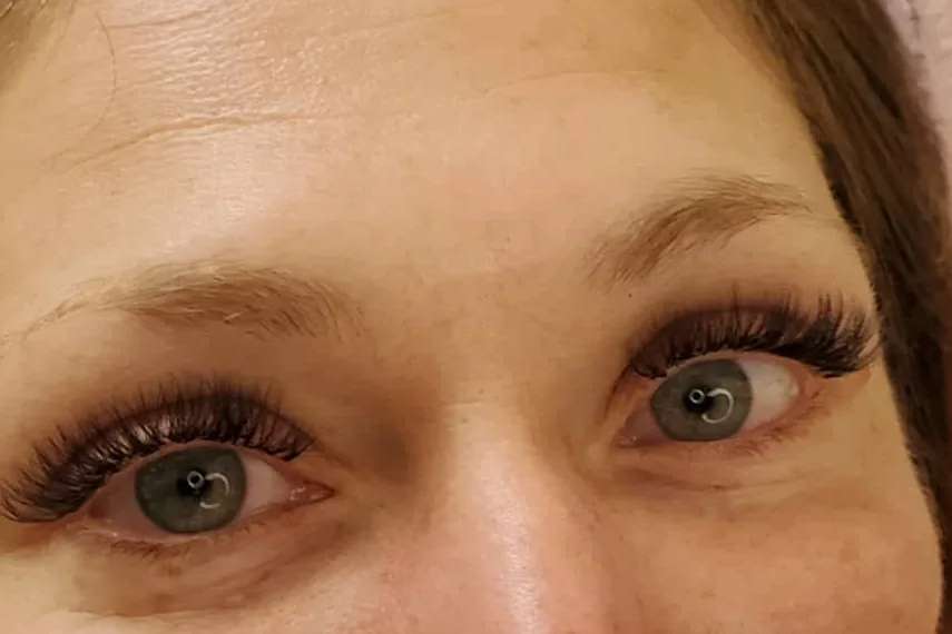Full, fluffy lash extensions on a client's open eyes, with her brows above