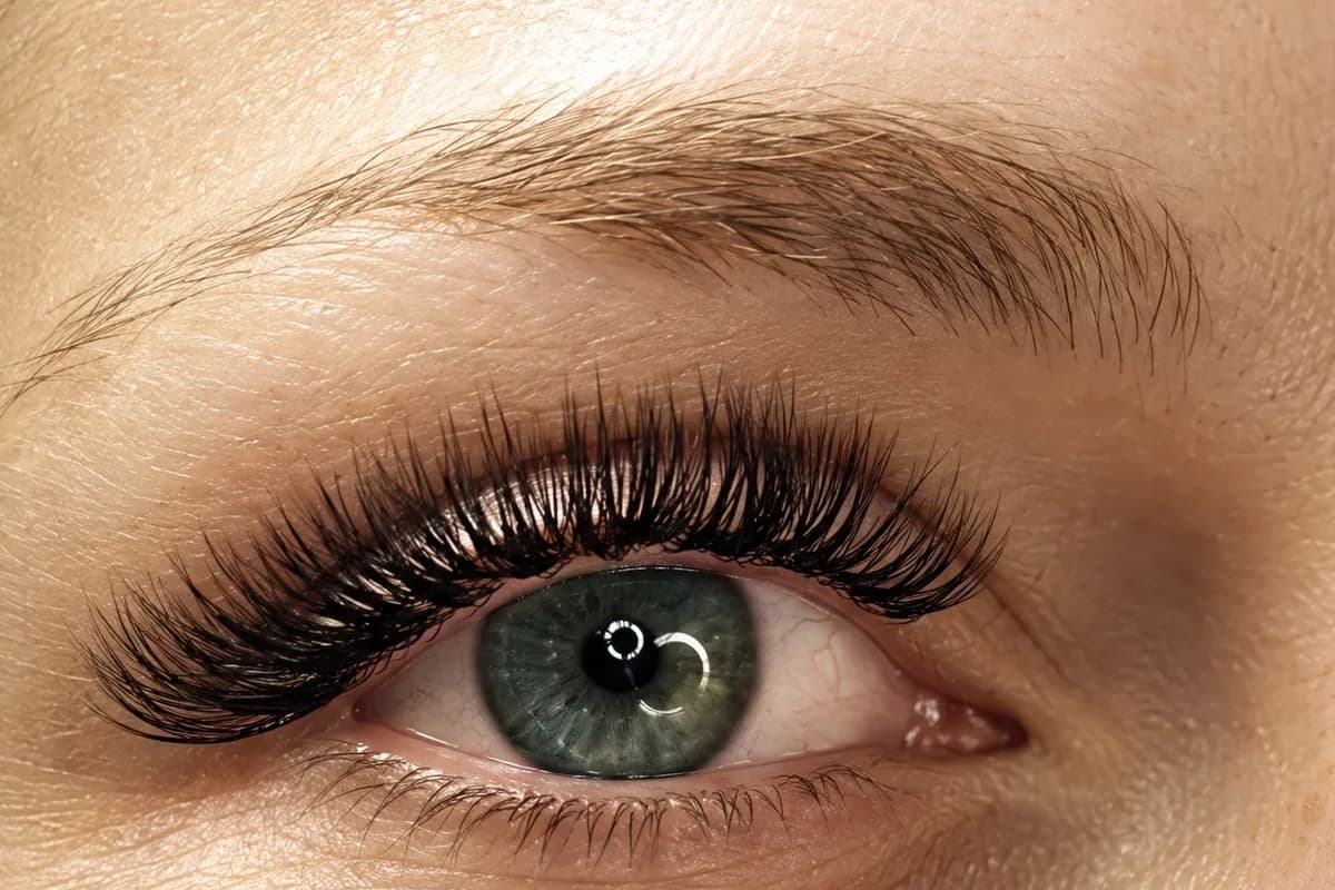 Full, dark lash extensions on an open green eye glancing up, under a soft, brushed brow